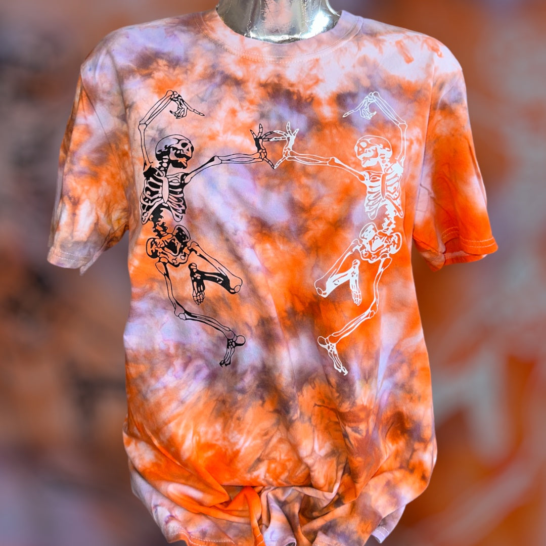 A short-sleeve tie-dye t-shirt displayed on a mannequin torso. The shirt features a vibrant orange, purple, and white tie-dye pattern with black and white skeleton graphics dancing in the center.