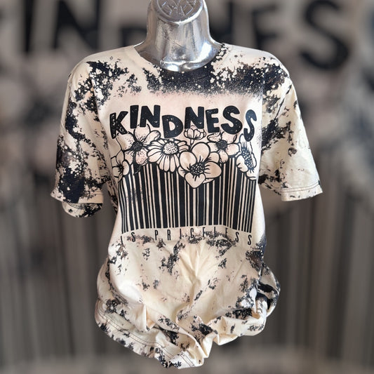 A short-sleeve graphic t-shirt displayed on a metallic mannequin torso. The shirt features a distressed black and cream bleach-splatter design with a central graphic containing the word 'KINDNESS' above a barcode and floral motif.