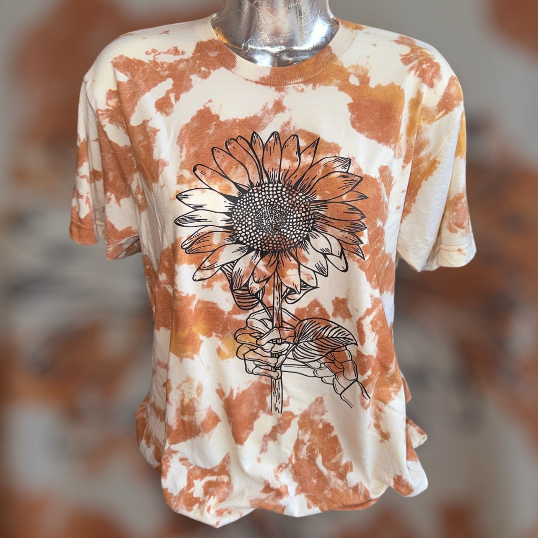 A short-sleeve crewneck t-shirt displayed on a silver mannequin torso. The shirt features a warm orange and cream tie-dye pattern with a large black line art graphic of a sunflower on the front.